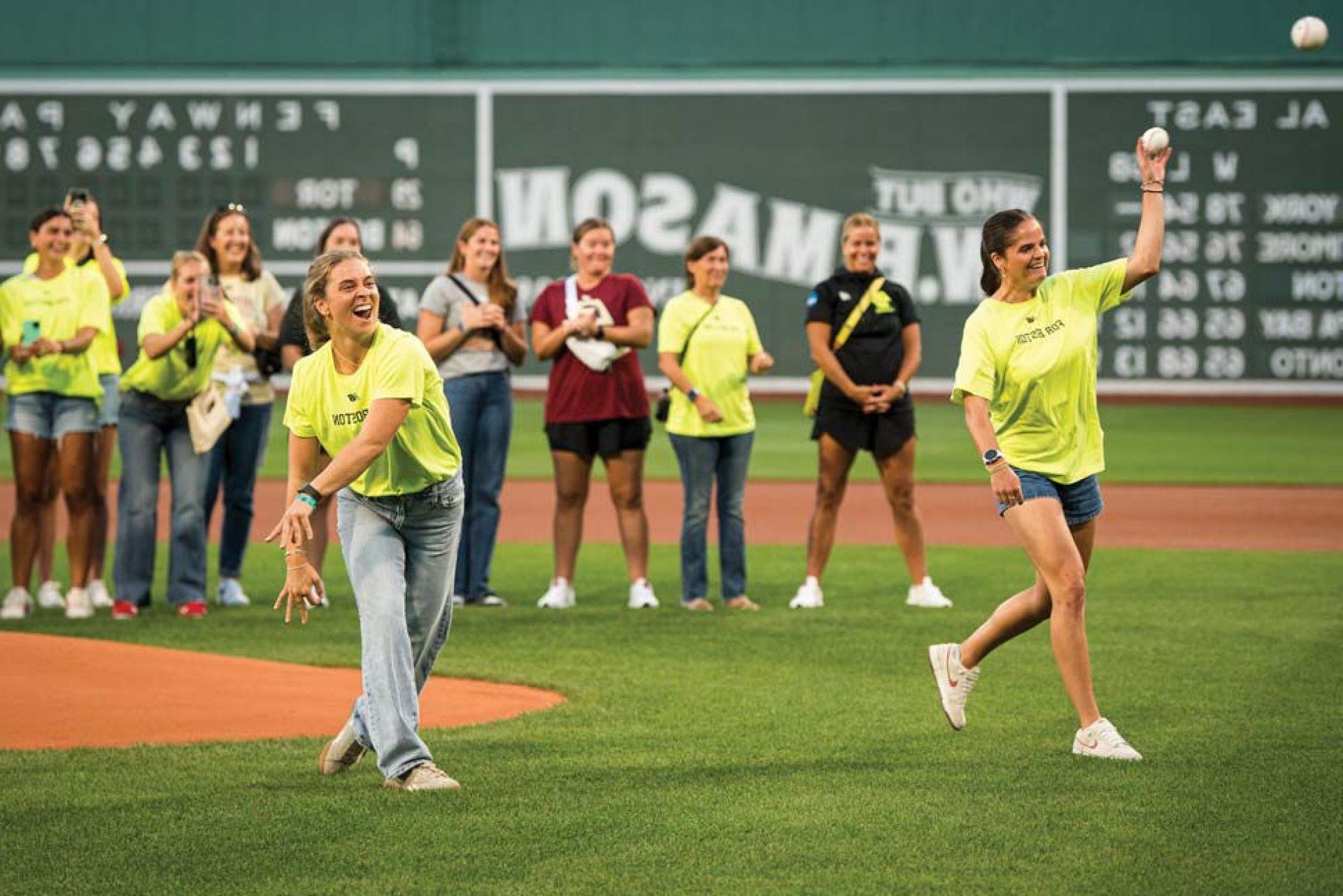 Two BC Lacrosse players throwing the first pitch with the team and coaching staff in the background