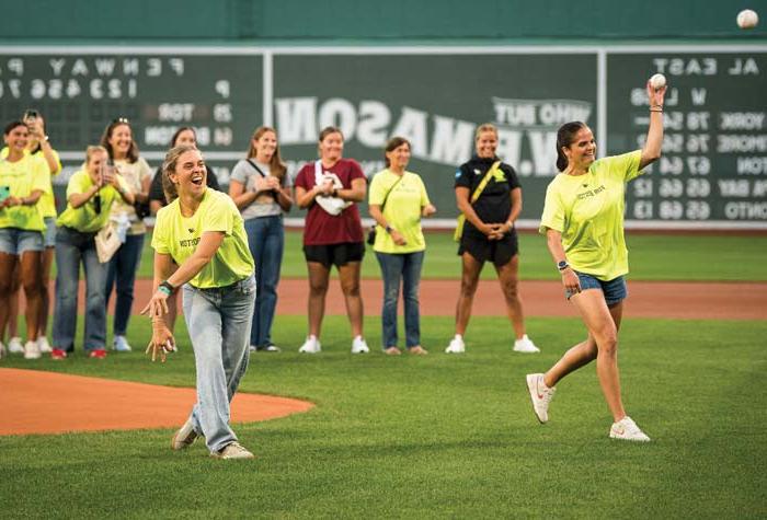 Two BC Lacrosse players throwing the first pitch with the team and coaching staff in the background